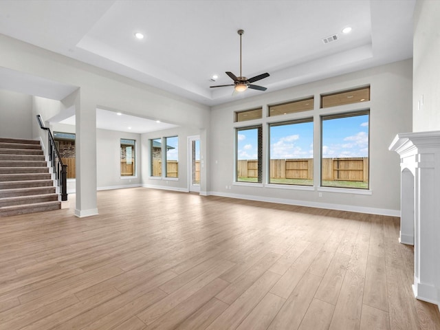 unfurnished living room with light hardwood / wood-style floors, a raised ceiling, and ceiling fan