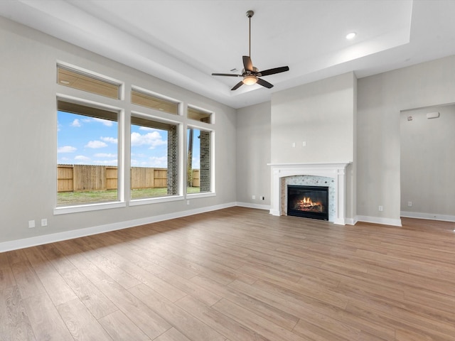 unfurnished living room with light wood-type flooring, a raised ceiling, and ceiling fan