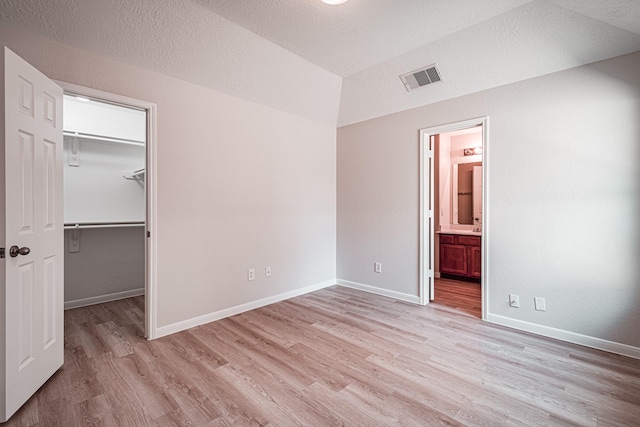 unfurnished bedroom featuring light wood-type flooring, a walk in closet, a closet, and connected bathroom