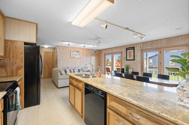 kitchen featuring wooden walls, sink, black appliances, and a textured ceiling