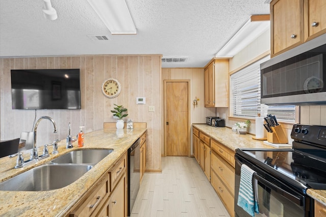 kitchen featuring wood walls, black appliances, sink, light stone countertops, and a textured ceiling