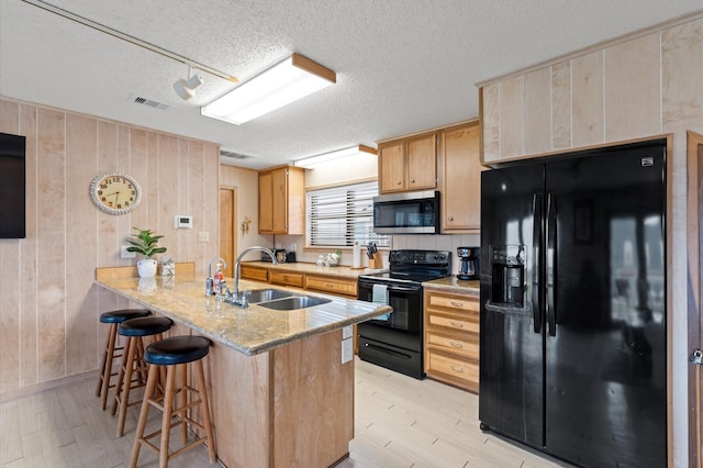 kitchen with black appliances, wood walls, sink, and a textured ceiling