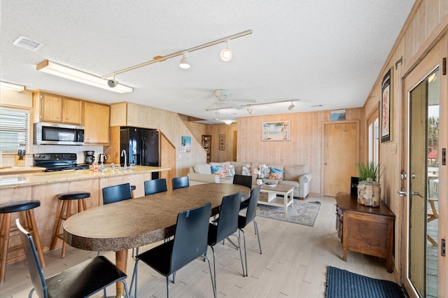 dining room featuring a textured ceiling, ceiling fan, wooden walls, sink, and light hardwood / wood-style floors