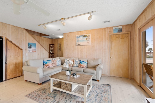 living room featuring wooden walls, ceiling fan, and a textured ceiling