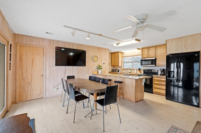 kitchen featuring kitchen peninsula, a textured ceiling, wooden walls, black appliances, and a breakfast bar area