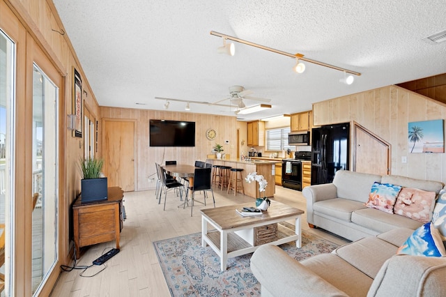 4406 Pabst Rd, Galveston, TX 77554 - living area with light wood-style floors, a ceiling fan, track lighting, wood walls, and a textured ceiling