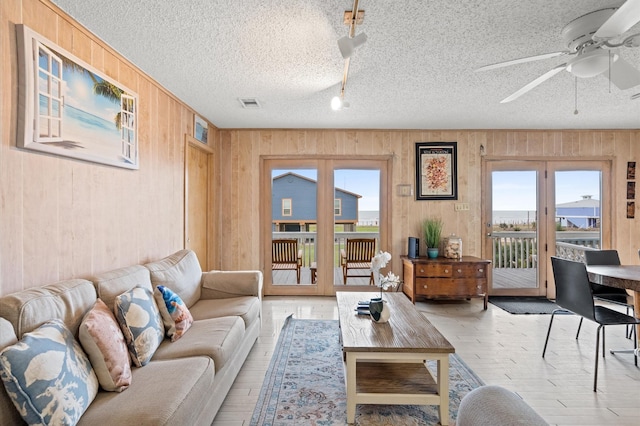 living room with french doors, a textured ceiling, ceiling fan, and wood walls