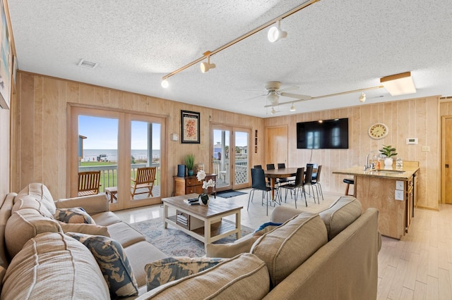 living room with wood walls, sink, ceiling fan, and track lighting