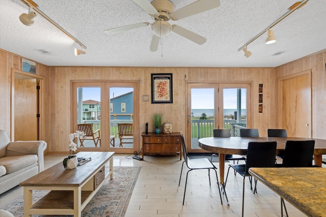 dining room featuring french doors, rail lighting, wooden walls, ceiling fan, and a textured ceiling