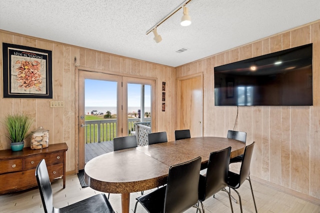 dining area featuring a textured ceiling, track lighting, and wood walls