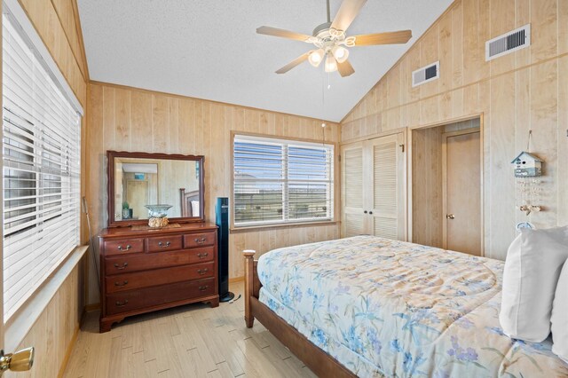 bedroom featuring ceiling fan, wood walls, lofted ceiling, and a closet