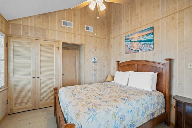 bedroom featuring wood walls, vaulted ceiling, ceiling fan, light hardwood / wood-style floors, and a closet