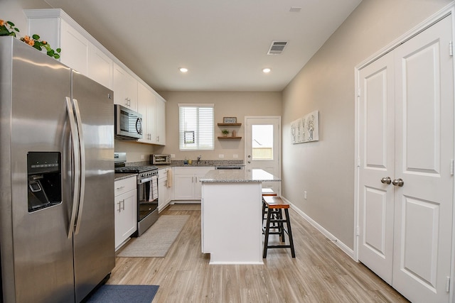 kitchen with light stone countertops, a center island, stainless steel appliances, a breakfast bar, and white cabinets