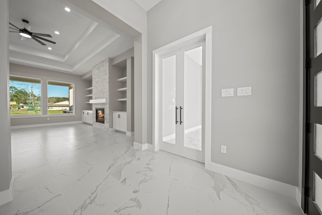 unfurnished living room with radiator heating unit, a fireplace, a raised ceiling, built in shelves, and french doors