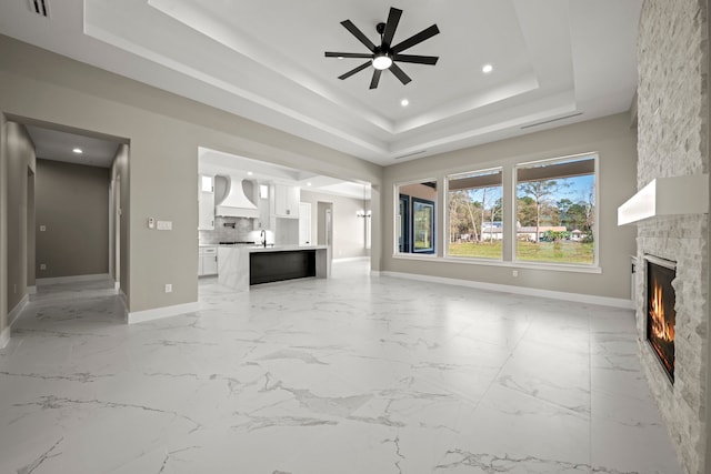 unfurnished living room featuring ceiling fan, a stone fireplace, and a raised ceiling