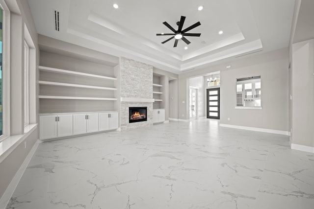 unfurnished living room featuring built in shelves, a fireplace, a raised ceiling, and ceiling fan with notable chandelier