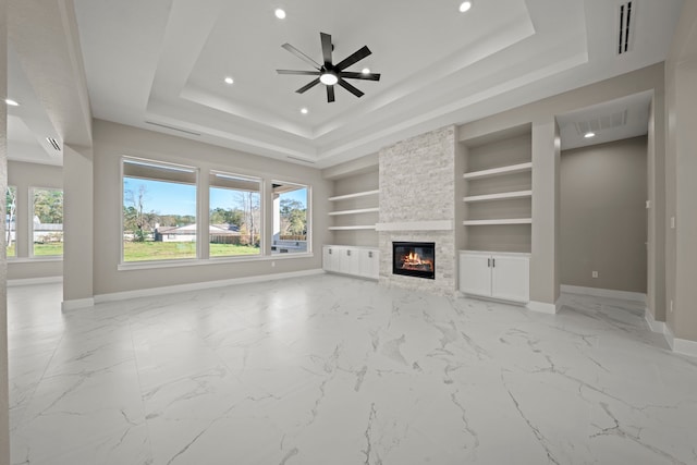 unfurnished living room featuring a raised ceiling, ceiling fan, a fireplace, and built in shelves