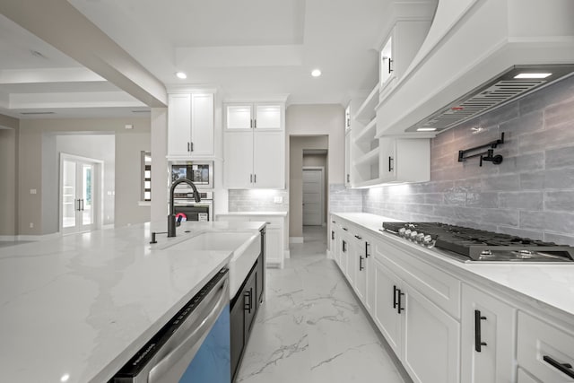 kitchen featuring sink, appliances with stainless steel finishes, white cabinetry, light stone countertops, and custom range hood