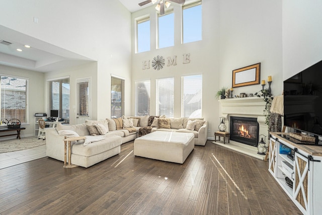 living room with dark wood-type flooring, ceiling fan, and a towering ceiling