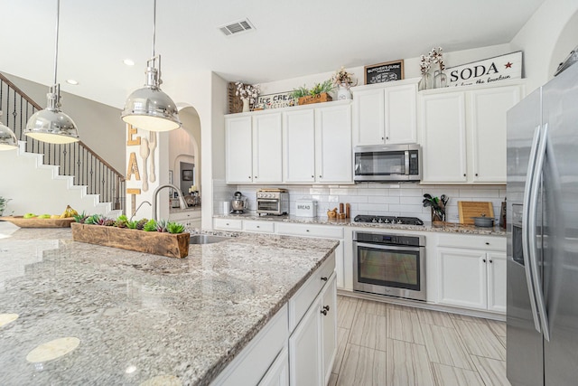 kitchen with appliances with stainless steel finishes, light stone countertops, decorative backsplash, and white cabinets