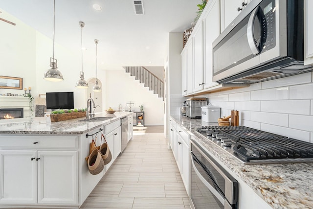 kitchen with white cabinetry, appliances with stainless steel finishes, decorative light fixtures, and light stone counters