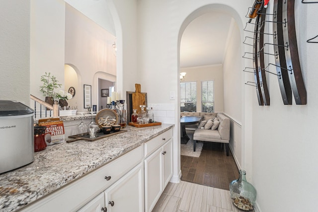 bar with white cabinetry, crown molding, and light stone counters