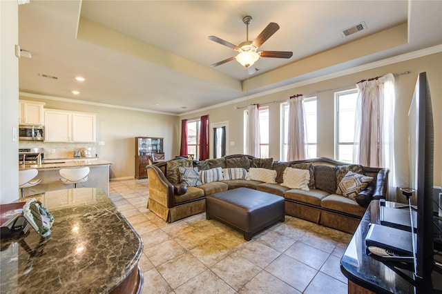 tiled living room with a raised ceiling, ceiling fan, and crown molding