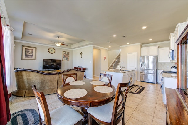 dining area featuring sink, ceiling fan, ornamental molding, light tile patterned floors, and a tray ceiling