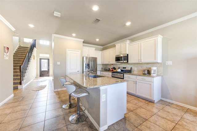 kitchen with a breakfast bar, stainless steel appliances, a kitchen island with sink, sink, and white cabinets