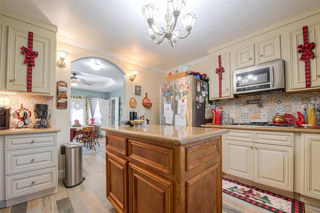 kitchen featuring tasteful backsplash, pendant lighting, appliances with stainless steel finishes, ceiling fan with notable chandelier, and light wood-type flooring