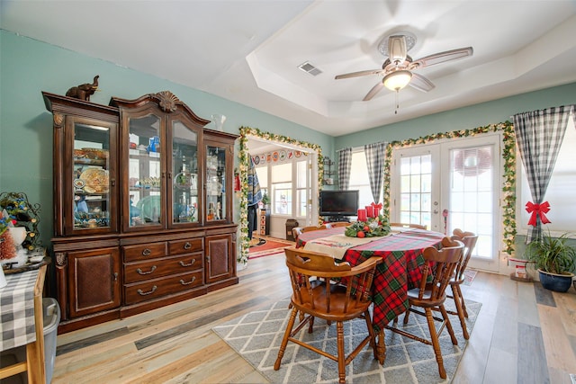 dining room with a tray ceiling, ceiling fan, light hardwood / wood-style flooring, and french doors