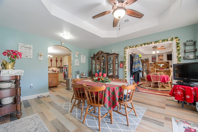 dining room featuring a fireplace, light wood-type flooring, a tray ceiling, and ceiling fan