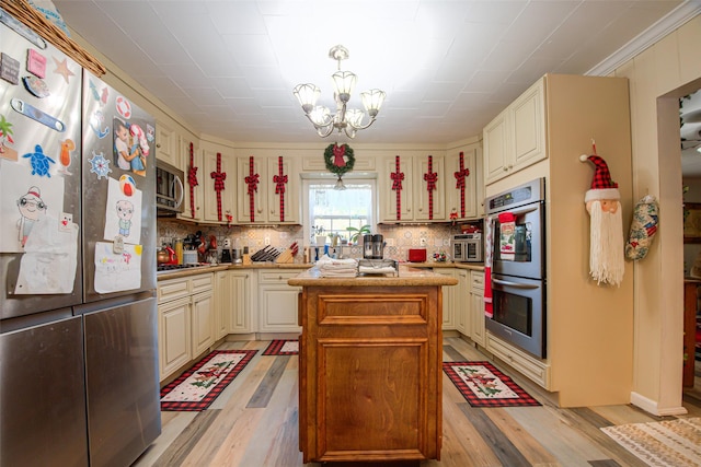 kitchen with an inviting chandelier, hanging light fixtures, light wood-type flooring, a kitchen island, and stainless steel appliances