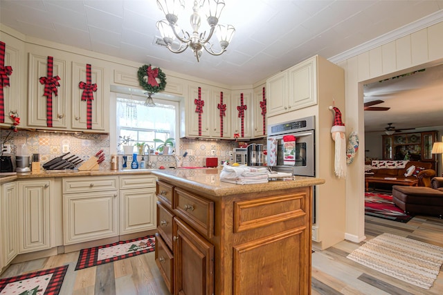 kitchen featuring stainless steel oven, ceiling fan with notable chandelier, hanging light fixtures, light hardwood / wood-style flooring, and light stone counters