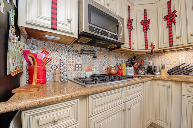 kitchen featuring backsplash, light stone countertops, cream cabinets, and stainless steel appliances