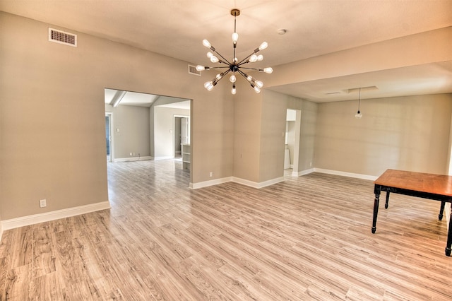 spare room with a notable chandelier and light wood-type flooring