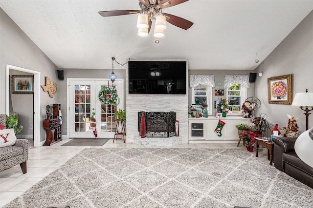 tiled living room featuring ceiling fan, a large fireplace, lofted ceiling, and french doors