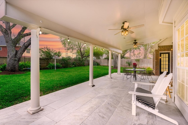 patio terrace at dusk with ceiling fan and a yard