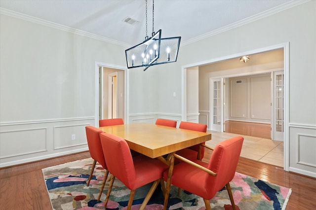 dining room with a chandelier, ornamental molding, light hardwood / wood-style flooring, and french doors