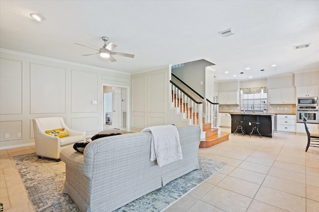 tiled living room with ceiling fan and crown molding