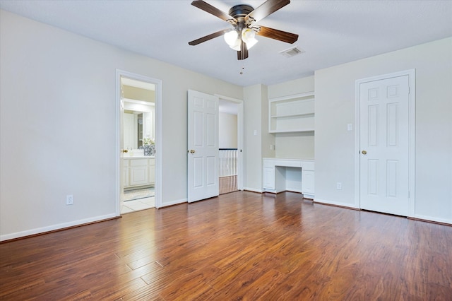 unfurnished living room with dark wood-type flooring, ceiling fan, built in desk, and built in shelves