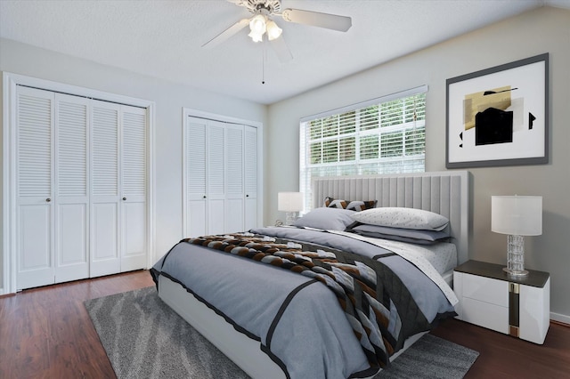 bedroom with ceiling fan, dark wood-type flooring, and two closets