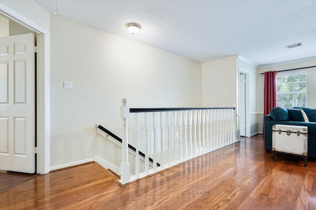 corridor featuring hardwood / wood-style floors, a textured ceiling, and ornamental molding