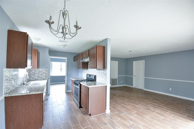 kitchen featuring tasteful backsplash, gas range, sink, a chandelier, and hanging light fixtures