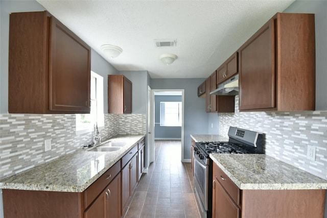 kitchen featuring backsplash, stainless steel gas range oven, light stone counters, and sink