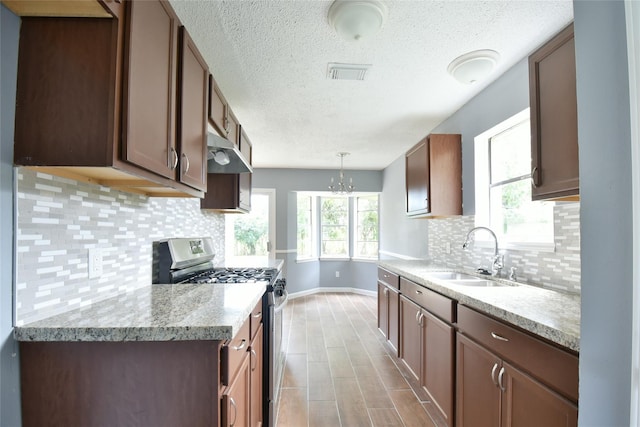 kitchen with backsplash, gas stove, sink, decorative light fixtures, and an inviting chandelier