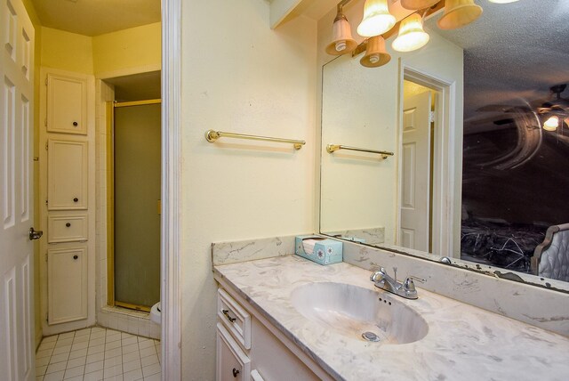 bathroom with a textured ceiling, tile patterned flooring, a shower stall, and vanity