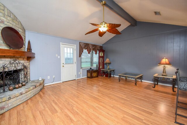 living room featuring vaulted ceiling with beams, light wood-style flooring, a brick fireplace, ceiling fan, and baseboards