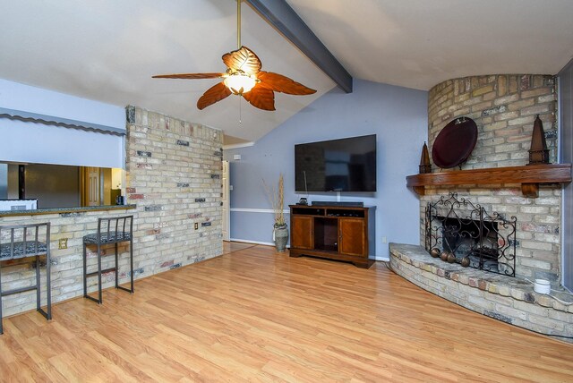 living room featuring vaulted ceiling with beams, ceiling fan, light wood-style flooring, baseboards, and a brick fireplace