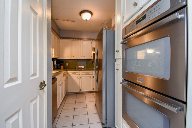 kitchen featuring light tile patterned floors, stainless steel appliances, light countertops, decorative backsplash, and white cabinetry